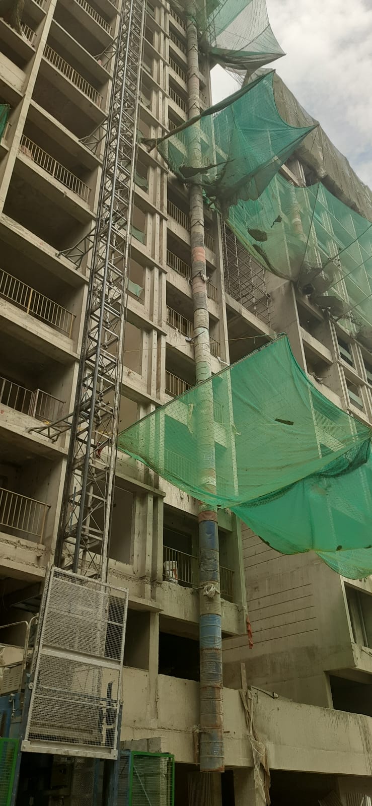 Building debris chute fitted alongside green safety netting on a high-rise project in Pune